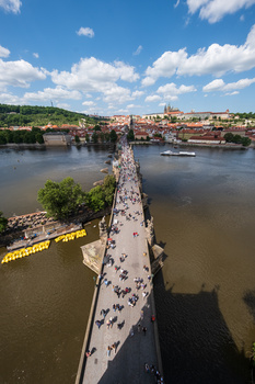 Elevated view of a crowded stone bridge spanning a wide river with a city in the background under blue sky.