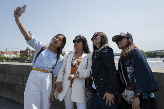 Four women posing together by a waterfront railing while one takes a selfie.