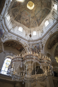 Ornate chandelier suspended in baroque church interior with domed ceiling and natural light from oculus.