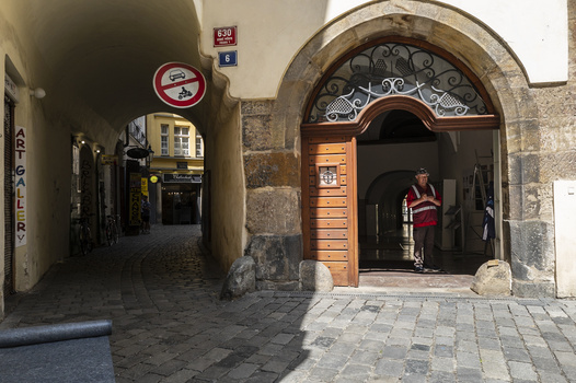 Narrow European alleyway with stone archway entrance and weathered facade lit by natural daylight.