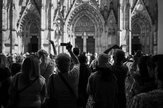 Crowd of people photographing ornate Gothic cathedral facade with phones and cameras raised.