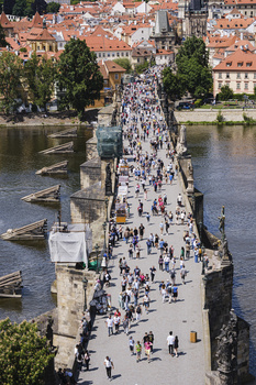 Aerial view of a historic stone bridge spanning a river, crowded with pedestrians, with terracotta-roofed buildings lining both riverbanks.