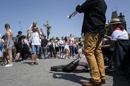 Street performer playing trumpet in front of gathered crowd on sunny day.
