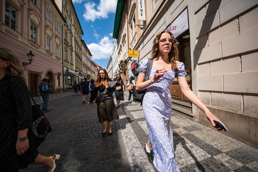 Woman in light blue dress walking down a European cobblestone street lined with buildings.