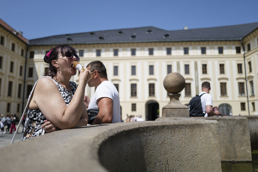 Woman in sunglasses resting her head on her hand at a stone ledge, with classical architecture in the background.