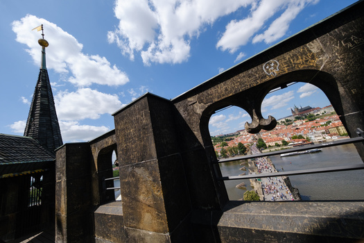 Stone archway frames a distant hillside city across a river under blue sky with white clouds.