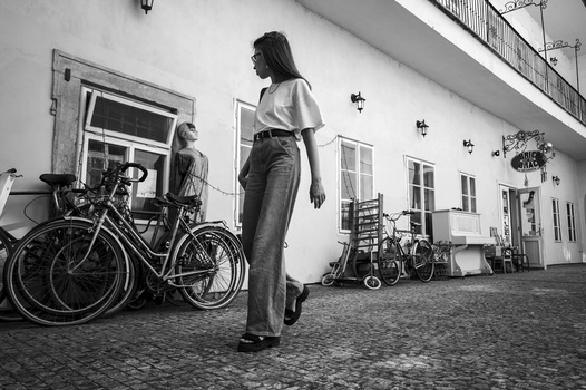 Woman in casual attire standing on a cobblestone courtyard near bicycles and a white building.