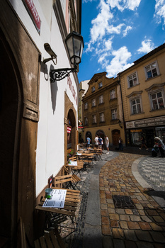 Narrow European street with historic buildings, cobblestone pavement, and bright blue sky with white clouds.