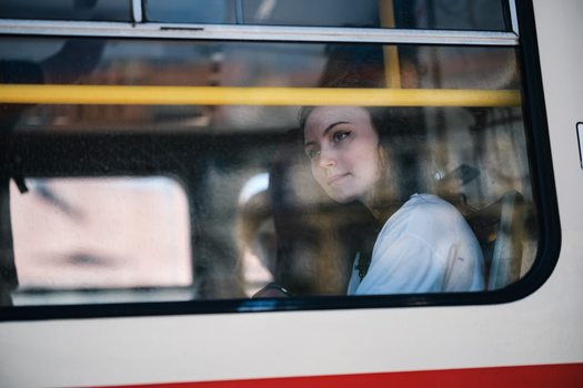 Woman looking out from inside a public transit vehicle through a window with yellow and red trim.