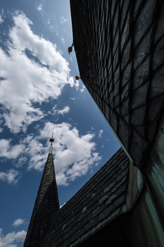 Upward view of modern skyscraper with sharp geometric angles against blue sky with white clouds.