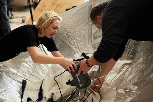 Two people assembling or adjusting a photography light modifier with white fabric stretched over a frame.