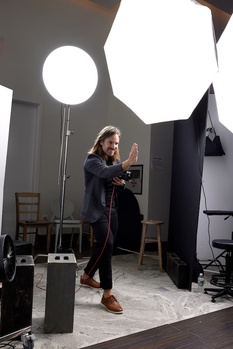 Photographer adjusting camera settings in a studio with large octabox and ring light fixtures overhead.