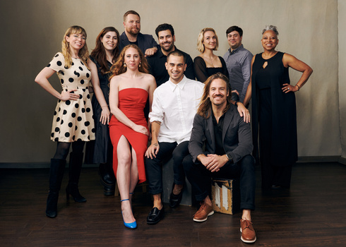 Group portrait of nine people arranged in two rows against a neutral beige backdrop.