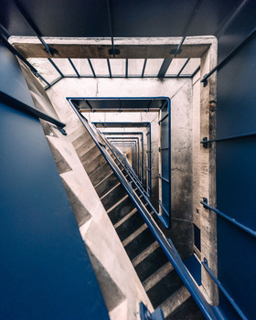 Overhead view of a concrete stairwell with blue walls descending into darkness, shot from directly above.