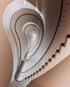Spiral staircase photographed from above, showing concentric white and wooden steps receding toward a vanishing point.