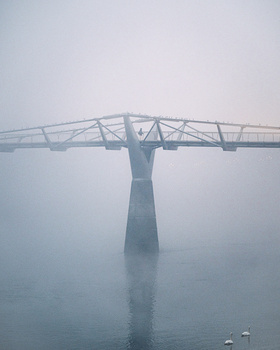 Millennium Bridge shrouded in thick fog, its steel cables and central support tower barely visible through heavy mist.