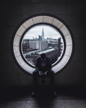 Silhouetted figure framed within a large circular architectural opening, viewing an urban cityscape beyond.