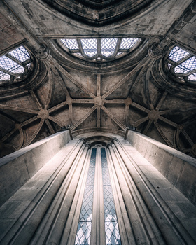 Symmetrical upward view of a Gothic cathedral ceiling with ribbed vaults and pointed arches converging toward a central window.