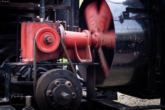 Red industrial fan or blower mechanism mounted on dark machinery with a large spinning rotor blade visible.