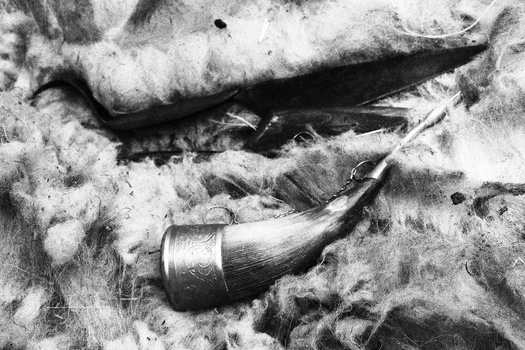 Weathered smoking pipe and curved knife blade partially buried in sand and earth.