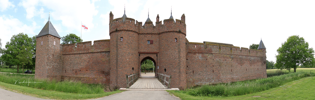 Medieval brick fortress with crenellated towers and central gatehouse, approached via wooden drawbridge.