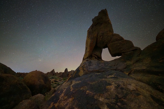 Natural rock arch formation silhouetted against a starry night sky in a desert landscape.