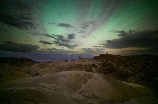 Desert landscape at twilight with aurora-like green sky and rolling sand formations.