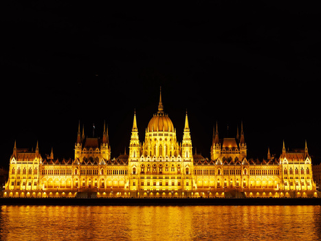 Illuminated Gothic Revival parliament building reflected in calm water at night.