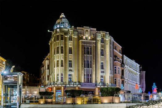Ornate art deco building illuminated at night with golden and blue lighting against dark sky.