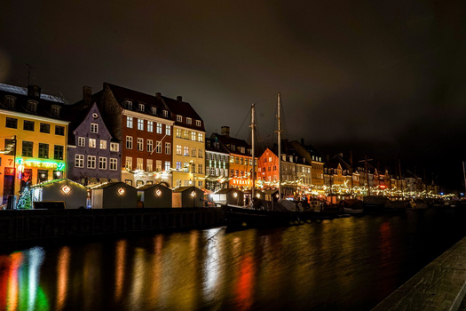 Historic waterfront buildings illuminated at night with reflections in calm water below.