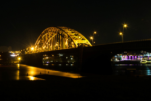 Illuminated arch bridge spanning dark water at night with warm yellow lighting and street lamps.