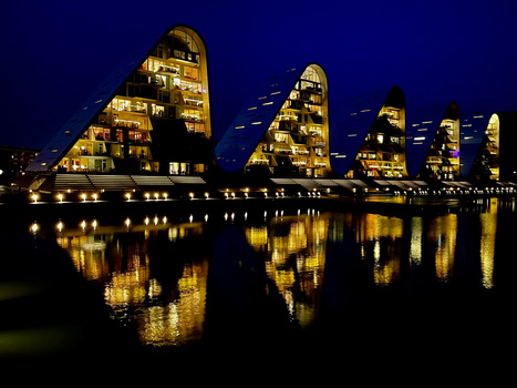 Row of illuminated residential buildings reflected in still water at night.