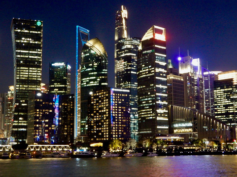 Illuminated skyscrapers reflected in dark water at night, featuring colorful accent lighting on tower facades.