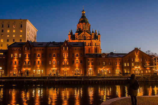 Illuminated Orthodox cathedral with golden domes reflected in still water at dusk.