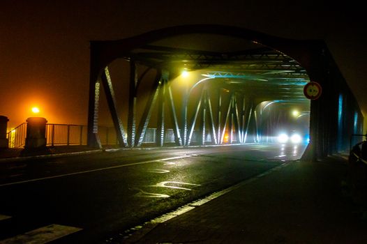 Industrial bridge interior at night illuminated by green and white LED lighting, with vehicle headlights visible.
