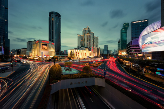 Urban intersection at dusk with light trails from traffic flowing through illuminated city streets.