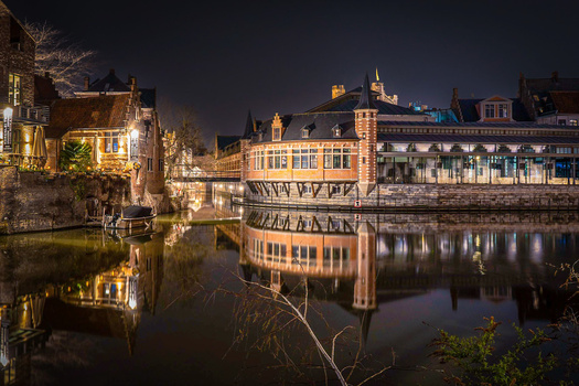 Historic waterfront buildings reflected in still water at night with warm architectural lighting.