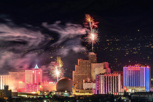Fireworks bursting over illuminated casino buildings at night with mountains in background.
