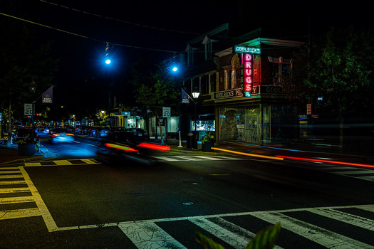 Nighttime urban street scene with light trails from moving vehicles crossing a crosswalk.
