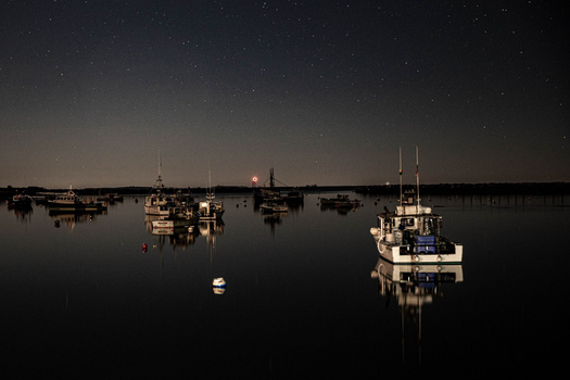 Fishing boats moored in calm water under a starlit night sky with subtle twilight glow on the horizon.