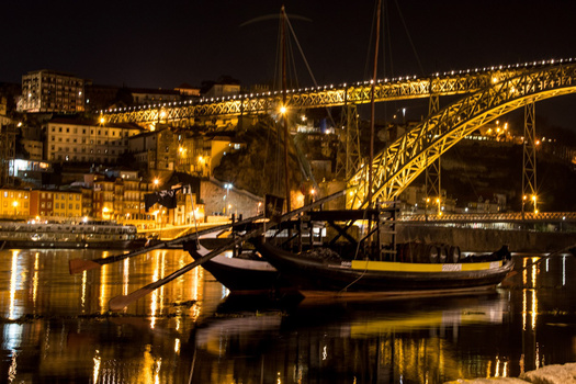 Traditional wooden boat moored in calm water at night beneath an illuminated arched bridge.
