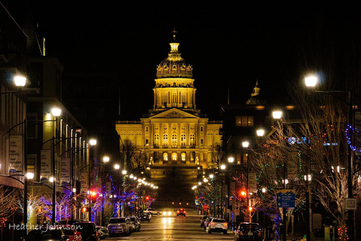 Illuminated capitol building at night centered on a tree-lined avenue with purple holiday lights.
