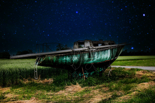 Abandoned fishing boat lit with green underglow against a starry night sky and grassy field.