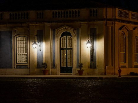 Nighttime architectural photography of an ornate building facade with illuminated golden walls, arched doorway, and hanging lanterns.