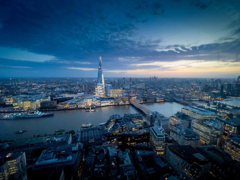 London cityscape at twilight with illuminated Shard tower reflected in Thames River.