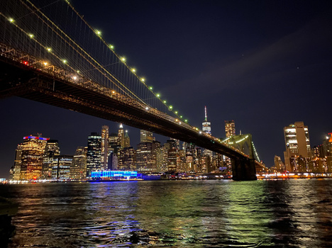 Brooklyn Bridge spanning the East River at night with Manhattan skyline illuminated in the background.