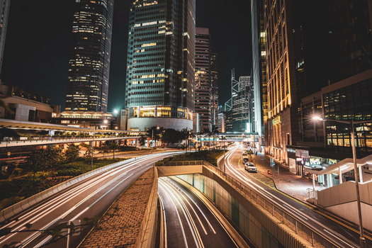 Long exposure urban highway at night with light trails beneath illuminated skyscrapers.