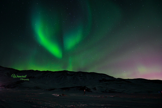 Northern lights displaying vibrant green aurora borealis above a dark mountainous landscape at night.