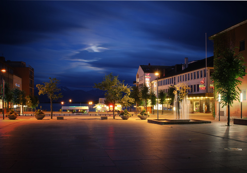 European town square at twilight with warm street lighting and historic buildings reflected on wet pavement.
