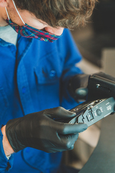 Technician in blue jacket and black gloves examines a handheld digital device with focus on the screen.